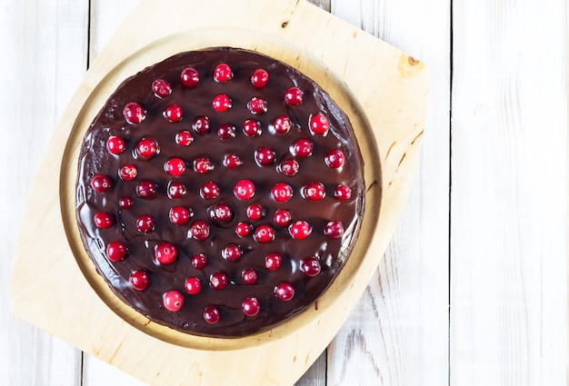 Brownie cake with chocolate icing, decorated with cranberries, on a light wooden table. Gluten-free. Healthy Dessert