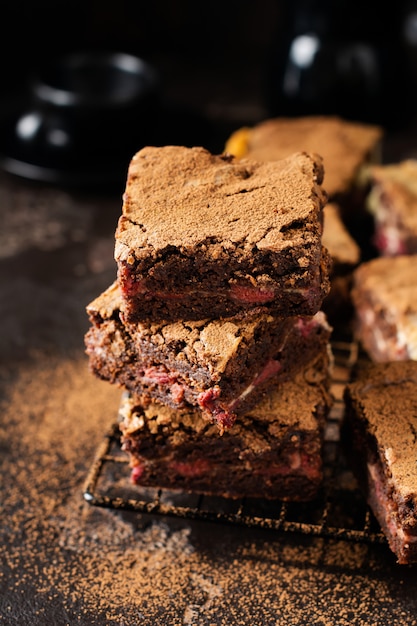 Brownie cheesecake cake with cherry and chocolate on a dark background. Selective focus.