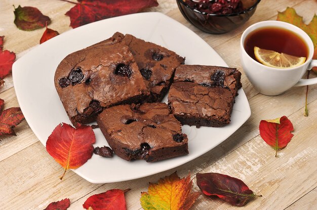 Brownie pieces with cherries on a wooden background with autumn leaves