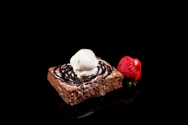 Brownie with ice cream and strawberries on a black background