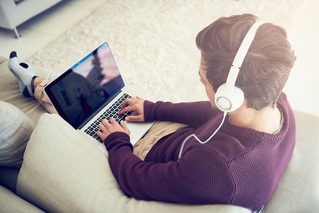 최신 음악 검색 집에 있는 소파에 앉아 노트북으로 음악을 듣는 젊은 남자의 하이 앵글 샷