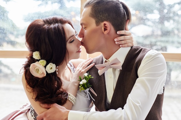 Bruid en bruidegom in de buurt van groot raam knuffelen voor bruiloft. Liefde en tederheid in elke look. Paar verliefd zoenen thuis. Een man geeft een vrouw een boeket bloemen. Rusland, Sverdlovsk, 20 april 2018