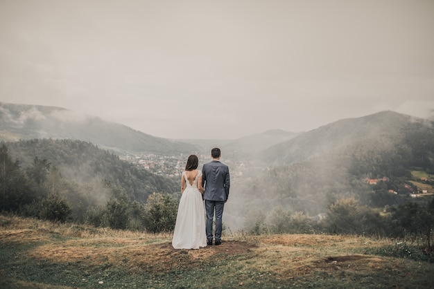 Bruid en bruidegom kijken naar het bos in de bergen in de mist