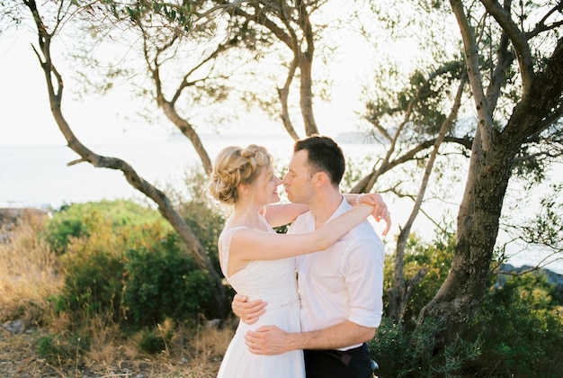 Bruid en bruidegom knuffelen en kussen bijna onder een boom