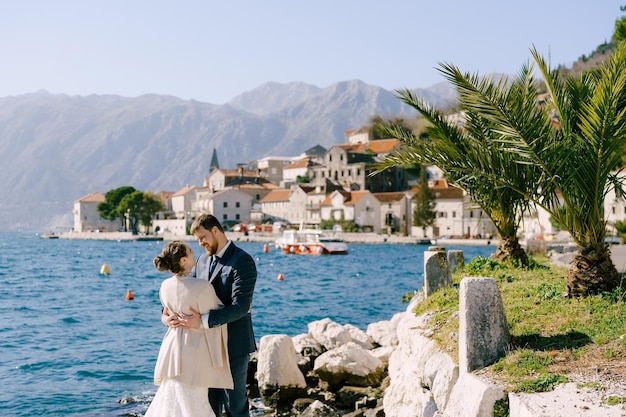 Bruid en bruidegom knuffelen terwijl ze op de stenen voor de kust van perast montenegro staan