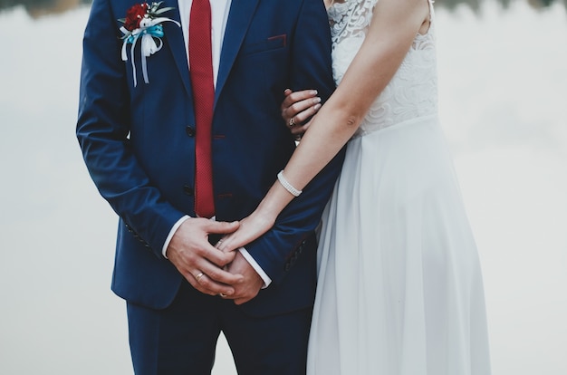 Bruid en bruidegom omhelzen elkaar. Blauw herenkostuum met donkerrode stropdas en witte kanten chiffon jurk.