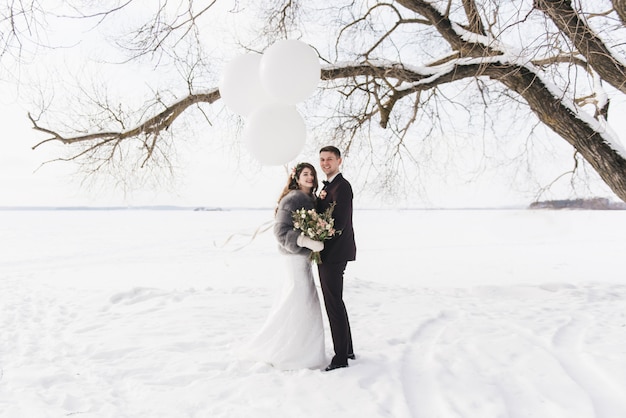 Bruid en bruidegom onder besneeuwde landschap met grote witte ballonnen