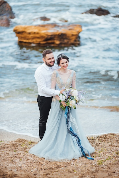 bruid in een blauwe jurk loopt langs de oceaankust