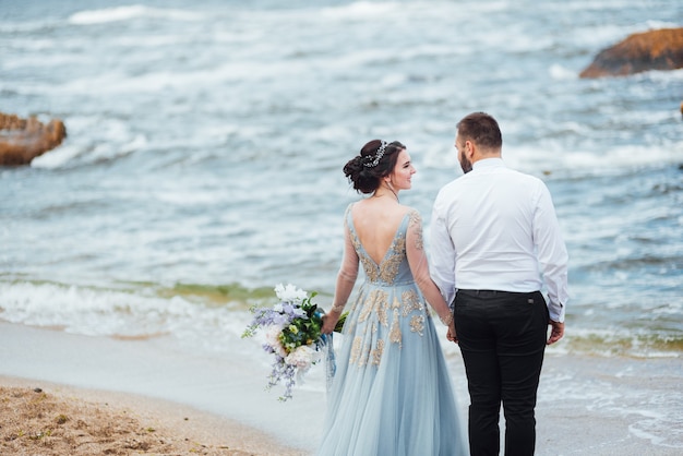 bruid in een blauwe jurk loopt langs de oceaankust