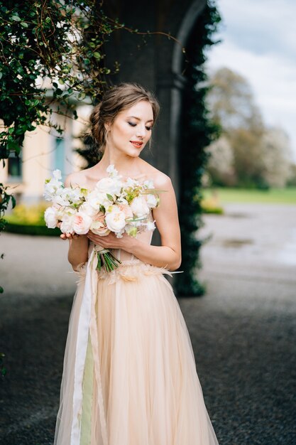 Bruid in een mooie jurk met blote schouders houdt een boeket roze bloemen vast