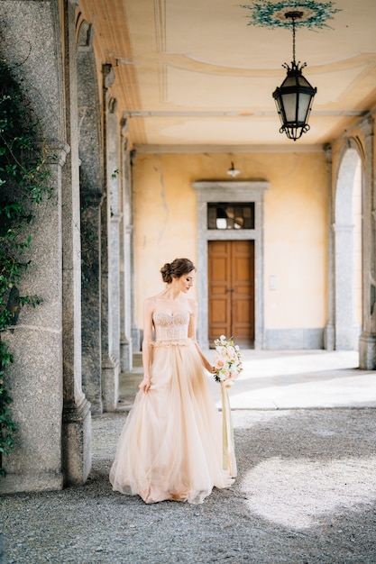 Bruid in een mooie jurk met een boeket roze bloemen staat in een gewelfde gang