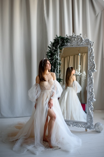 bruid in een trouwjurk staande naast een spiegel versierd met kerstdecor.