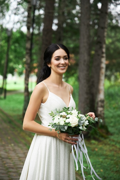 Bruid in mooie witte jurk en boeket bloemen in haar handen