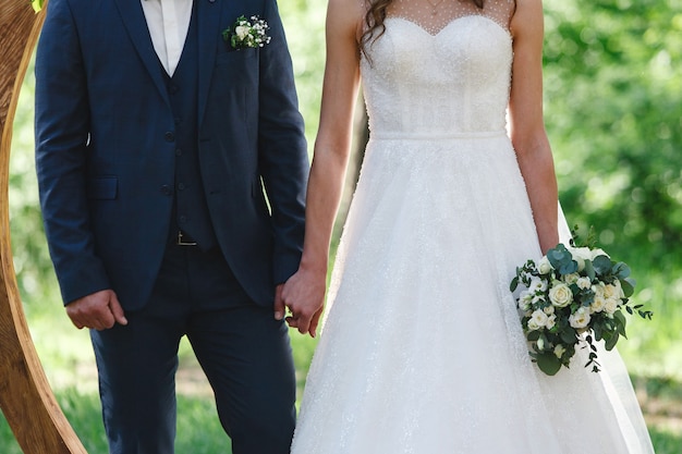 Bruid in witte jurk met mooi boeket en bruidegom hand in hand buiten bij huwelijksceremonie