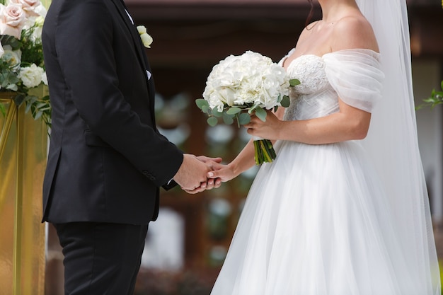 bruid in witte jurk met mooi boeket van witte rozen en bruidegom op de huwelijksdag van de huwelijksceremonie