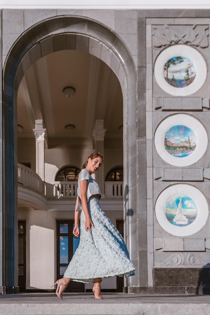 Bruid in zacht turquoise tafzijden jurk danst op de veranda van het gebouw met originele architectuur