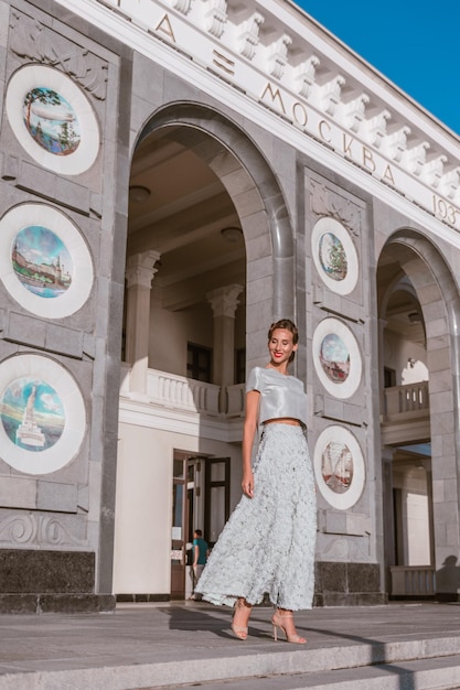 Bruid in zacht turquoise tafzijden jurk danst op de veranda van het gebouw met originele architectuur