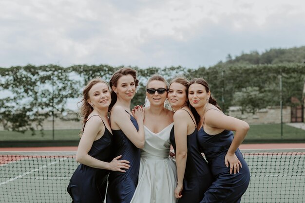 Bruid met de bruidsmeisjes in de glanzende jurken op de tennisbaan