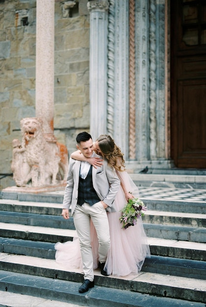 Bruid omhelst bruidegom van achteren bij de schouders staande op de trap bergamo italië