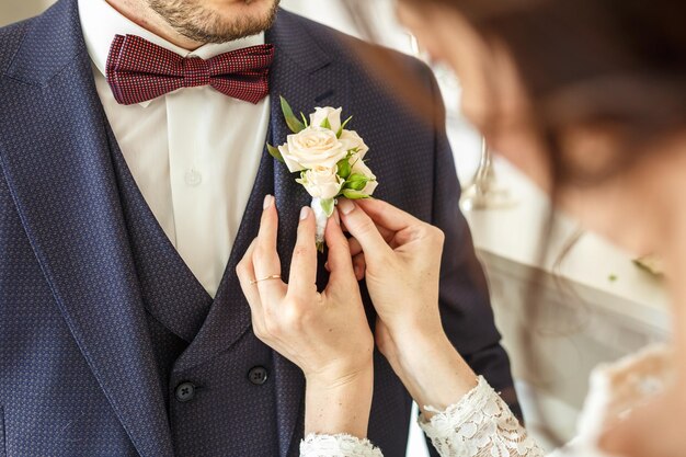 Bruid zet bruidegom op boutonnière van witte rozen op trouwdag