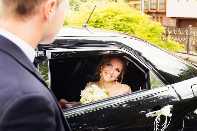 Bruid zit in een zwarte auto en kijkt door een raam naar haar verloofde
