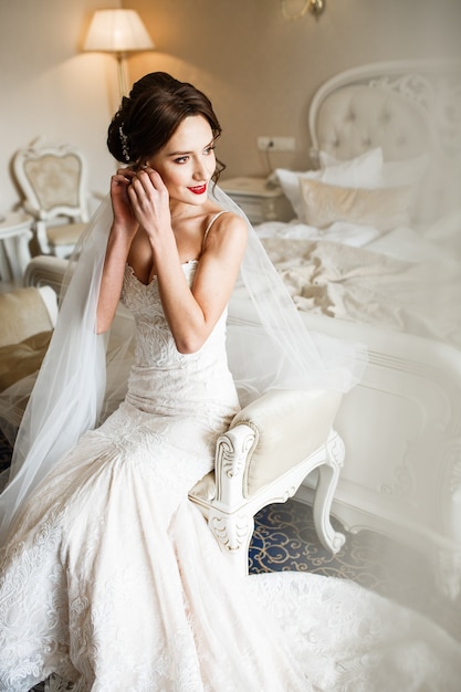 Foto bruid zit in trouwjurk op kleine witte sofa
