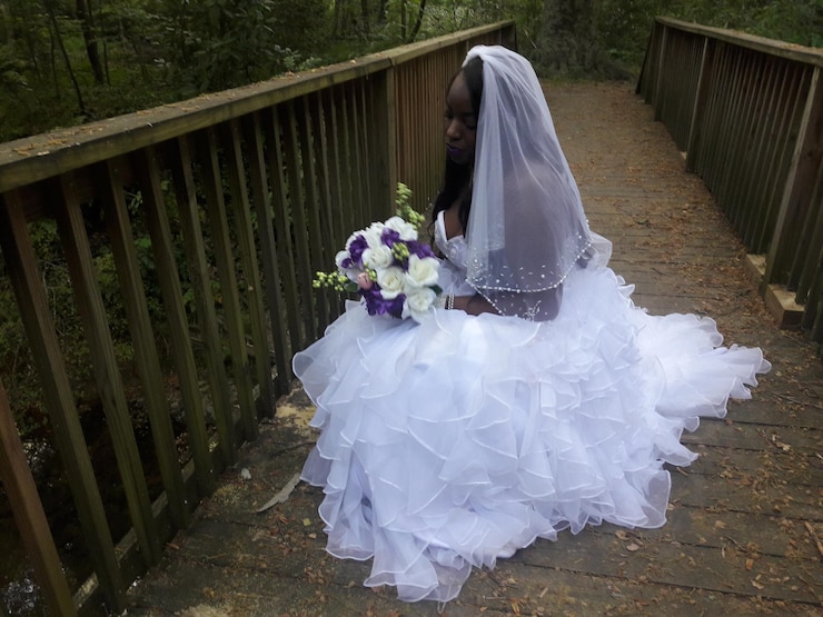 Foto bruid zit op een voetgangersbrug in het bos.