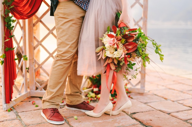 Bruidegom en bruid met een boeket bloemen staan op een stenen tegel tegen de achtergrond van een gesneden