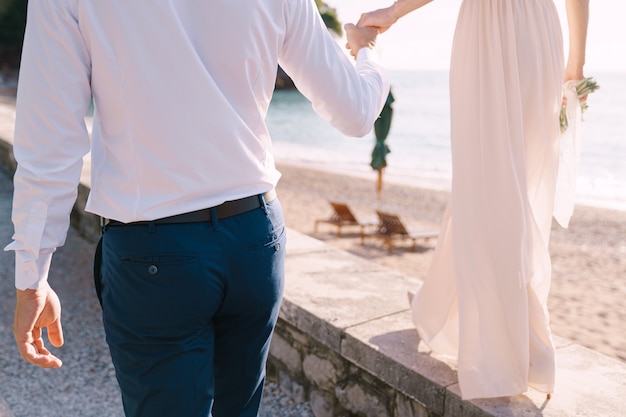 Bruidegom houdt de hand van de bruid vast met een boeket dat langs de kust loopt