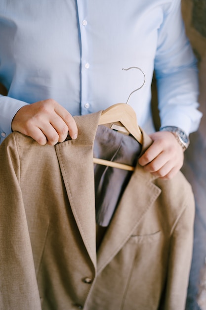 Bruidegom in een blauw shirt houdt een bruin jasje aan een hanger