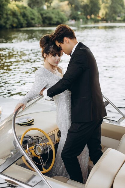 Bruidegom in een zwart pak en zonnebril knuffelt bruid in trouwjurk op een jacht op een zonnige dag