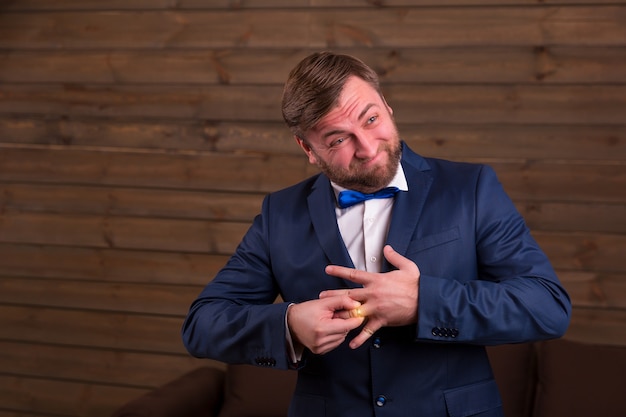 Bruidegom in pak en vlinderdas die een trouwring om zijn vinger op houten kamer probeert te zetten