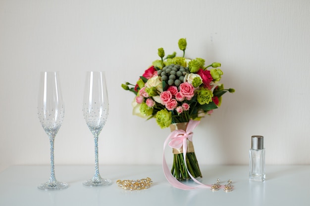 Bruids mooi romantisch boeket van verschillende bloemen, glazen voor champagne, in schitterende stenen, een gouden haarspeld, oorbellen. Selectieve aandacht.