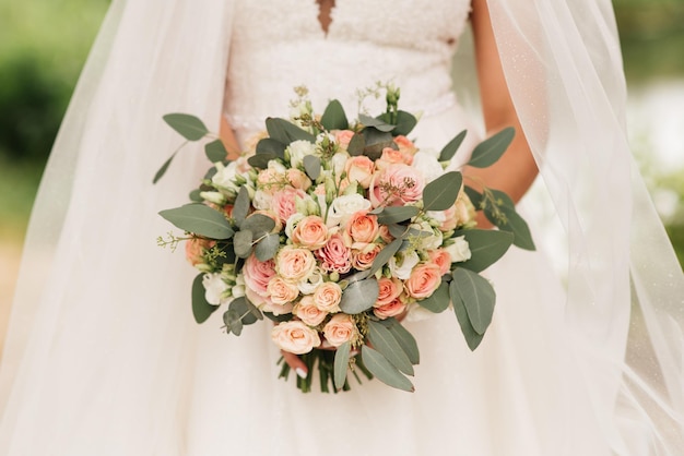 Bruidsboeket in pastelkleuren in de handen van de bruid van rozen eustoma pioenrozen anjers en eucalyptus