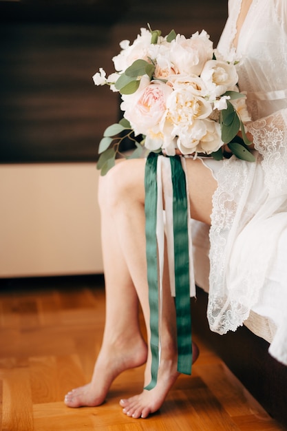 Bruidsboeket van crèmekleurige rozen en eucalyptus liggend op de benen van de bruid tijdens de bijeenkomst voor de ceremonie