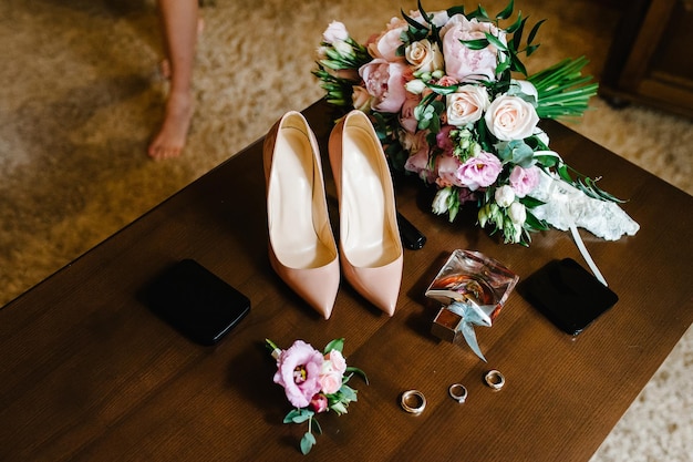 Foto bruidsboeket van de bruid van roze bloemen rozen en groen stijlvolle elegante klassieke gelakte beige schoenen parfums en gouden ringen