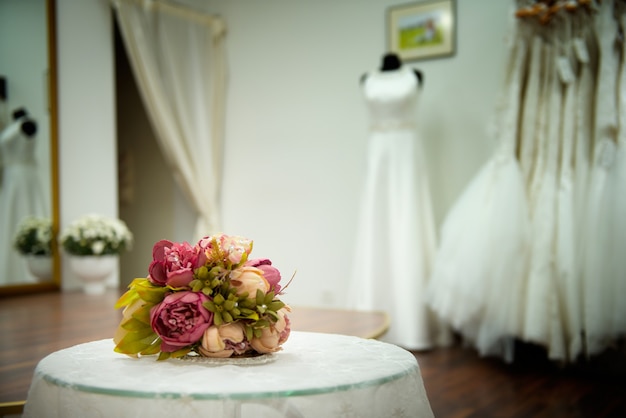 Bruidsboeket van rozen bloemen op tafel met kant in de trouwzaal in de buurt van witte jurken die wachten op de bruid