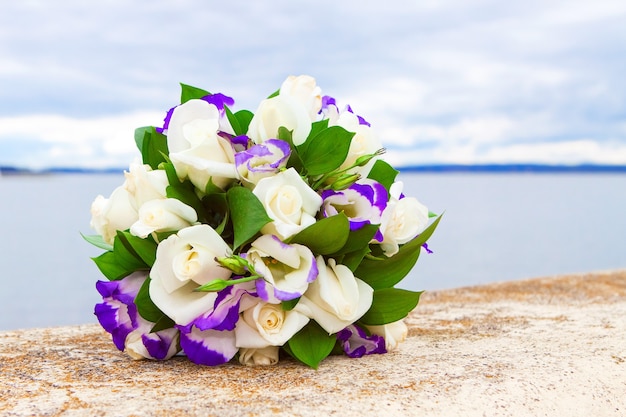 Bruidsboeket van witte roos in felle kleuren met paarse eustoma tegen het meer
