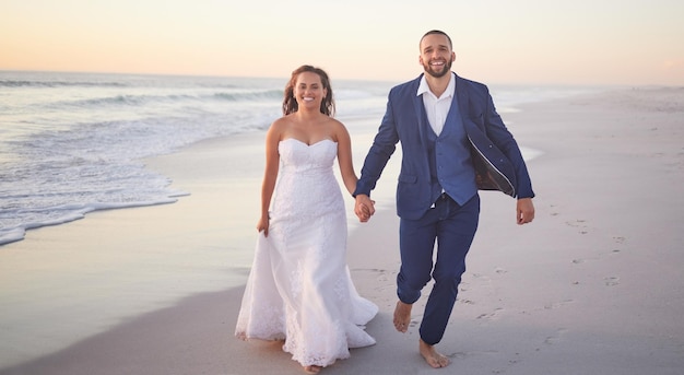 Bruidspaar en strand met een man en vrouw hand in hand tijdens het wandelen op het zand bij de oceaan of de zee Liefdesvertrouwen en huwelijk met een bruid en bruidegom aan de kust bij zonsondergang voor feest