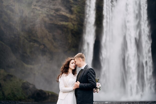 Bruidspaar in de buurt van skogafoss waterval bestemming ijsland bruiloft de bruid en bruidegom houden elkaars hand vast