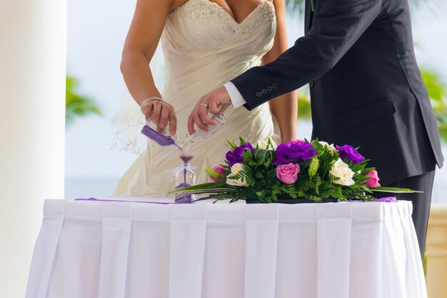 Bruidspaar praktijk mengen van zand ceremonie met bloemen boeket op tafel