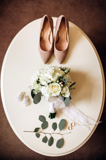 Bruidsschoenen met een boeket met rozen en andere bloemen op de fauteuil