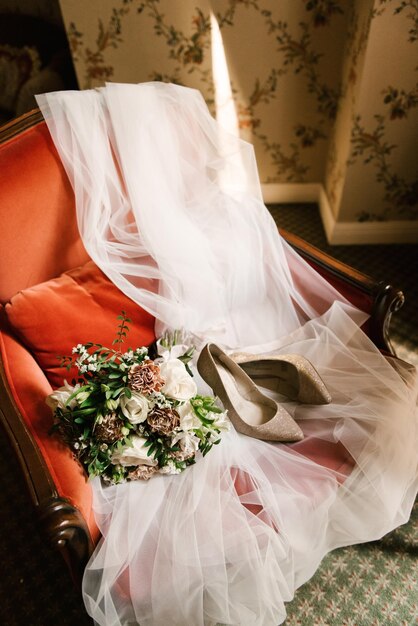Bruiloft accessoires van de bruid boeket schoenen sluier op een rode stoel