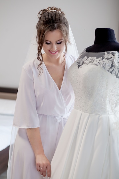 Bruiloft. Bruid in mooi gewaad in de buurt van de mannequin met jurk binnenshuis thuis. Trendy bruiloft stijl schot. Mode bruid.