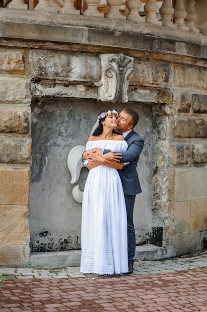 Bruiloft fotosessie op de achtergrond van het oude gebouw. De bruid en bruidegom omhelzen elkaar zachtjes.