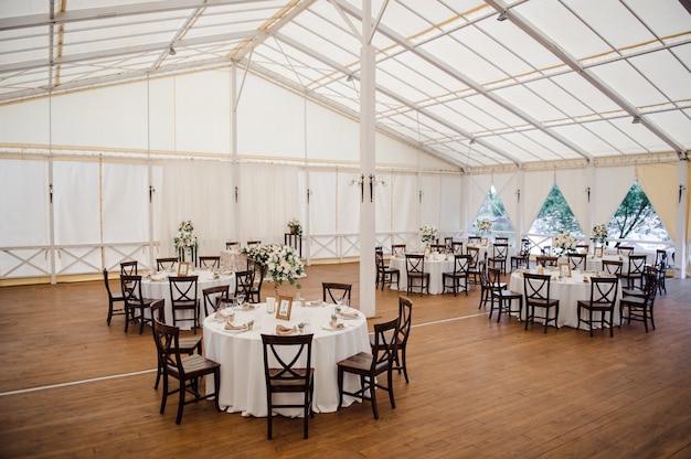 Bruiloft in een tent. Inrichting van de hal. Witte tafelkleden, mooi decor en gerechten.
