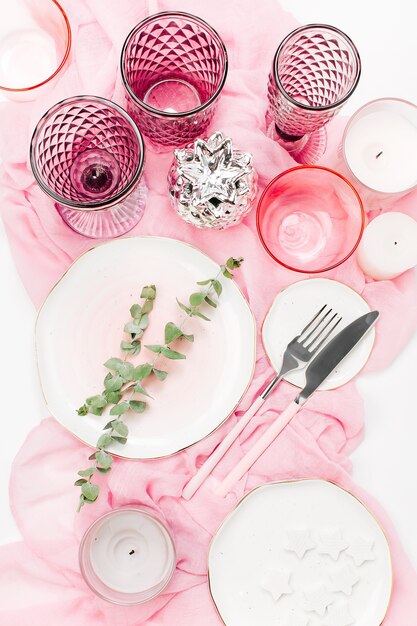 Bruiloft of feestelijke tafel setting. Borden, wijnglazen, kaarsen en bestek met decoratief textiel op witte achtergrond. Mooi arrangement op roze kleur