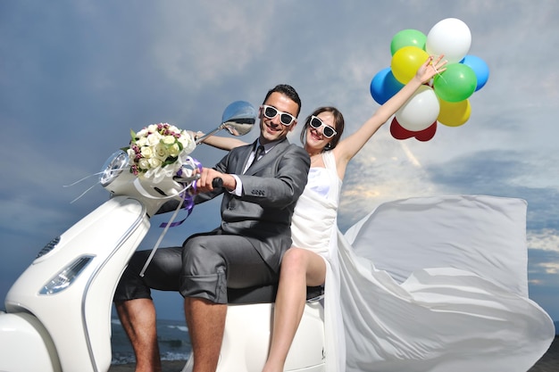 bruiloft sce van bruid en bruidegom net getrouwd stel op het strand rijden witte scooter en veel plezier