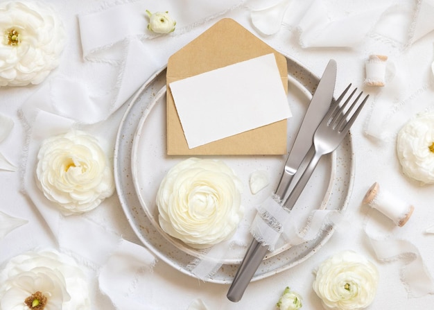Bruiloft tafel met kaart en envelop in de buurt van crème rozen en witte zijden linten bovenaanzicht mockup