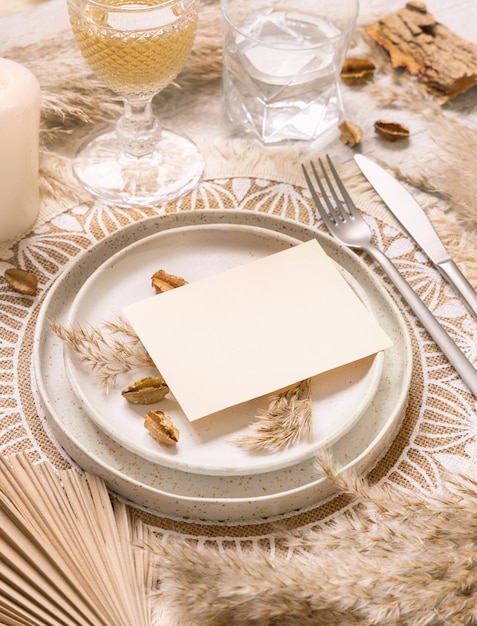 Bruiloft tafel plaats met horizontale lege kaart op Boheemse placemat close-up. Boho trouwkaart mockup. Tropisch beige sjabloon met gedroogde palmbladeren en pampagras, plaats voor tekst